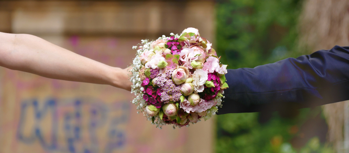 The arms of two people holding a bouquet. One is a bare arm and one is wearing a suit jacket.