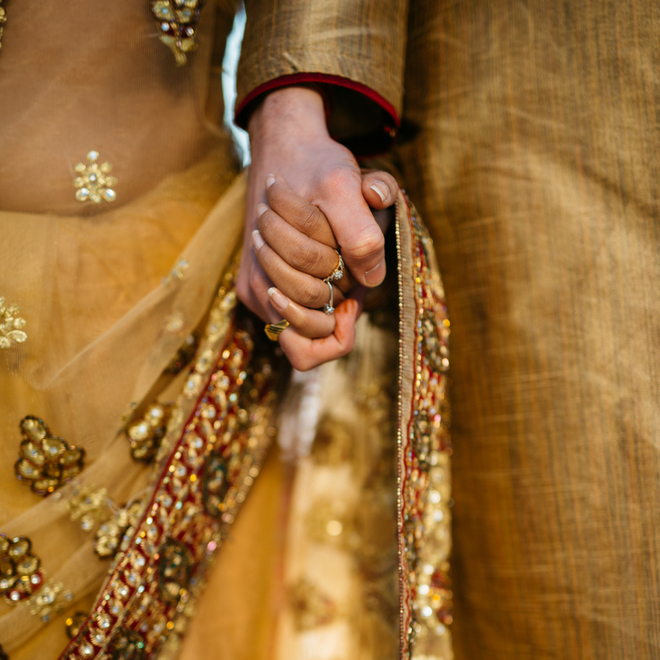 Close up of a man and a woman holding hands. They are wearing traditional Indian clothing.