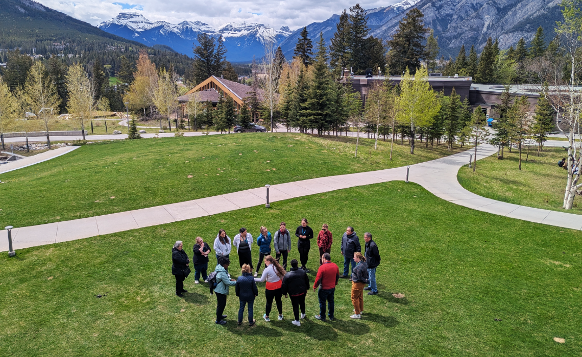 Participants gather at the large yarn at the Banff Systems Summit in the backdrop of breathtaking mountains with icy peaks and scattered green trees