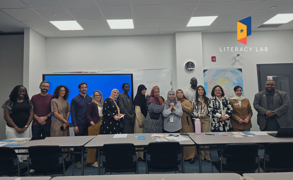 A diverse group of adults standing and smiling at the front of a classroom during a training session, with the Literacy Lab logo in the top right.