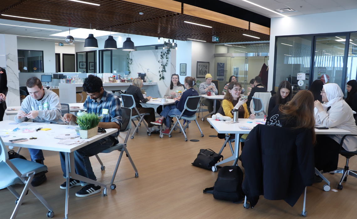Catamount fellows gathered in the Trico Changemakers Studio, working together on their crafts (beadwork) at tables with beads, papers, supplies, etc.
