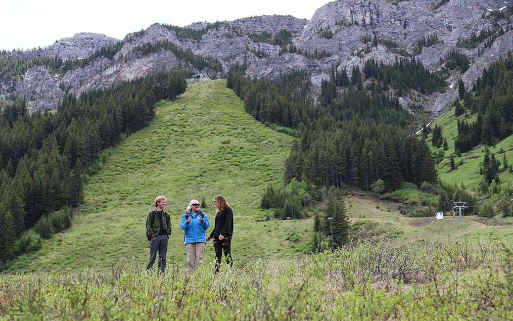 Three members of the Scotland Field School chatting and standing in a meadow below the Rocky Mountains